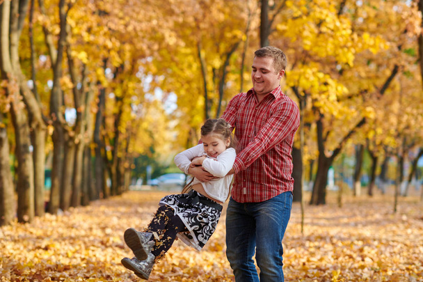 Padre e hija están jugando y divirtiéndose en el parque de otoño de la ciudad. Posan, sonríen, juegan. Árboles amarillos brillantes
. - Foto, imagen