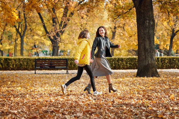 Two happy girls running in autumn city park. - Фото, зображення