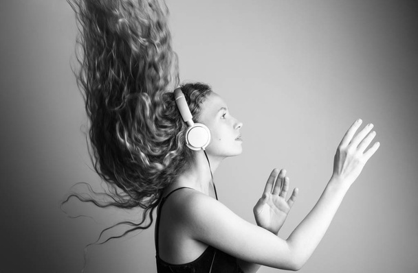Černobílý záběr krásná mladá žena poslechu hudby se sluchátky před bílou zdí - Fotografie, Obrázek