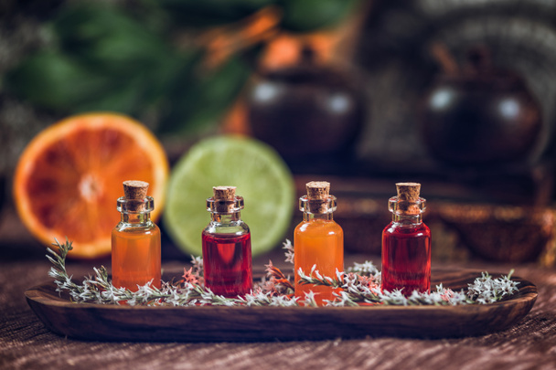 Пляшки наповнені червоними та оранжевими ефірними оліями на дерев'яній дошці. Свіжі цитрусові, апельсин і лайм розрізані навпіл. Ароматерапія концепція розслаблення
 - Фото, зображення
