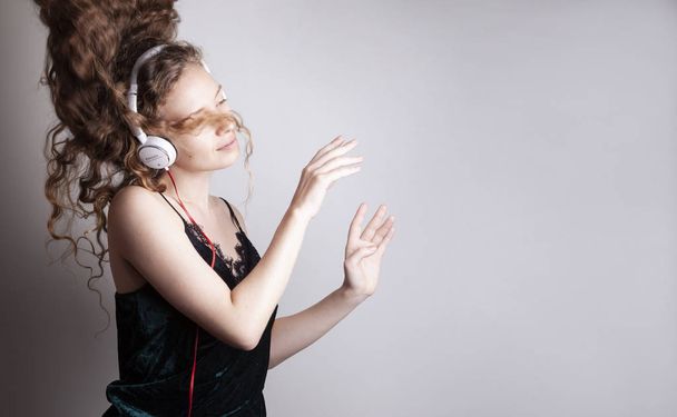 όμορφη νεαρή γυναίκα ακούτε μουσική με ακουστικά μπροστά από το λευκό τοίχο και χορό - Φωτογραφία, εικόνα