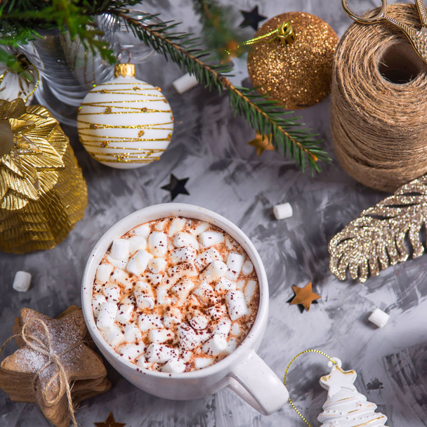 Uma grande xícara de cacau com marshmallow polvilhado com cacau em pó fica em uma mesa cinza entre decorações de Natal, ramos de abeto, biscoitos de gengibre e estrelas brilhantes. Vista superior
 - Foto, Imagem