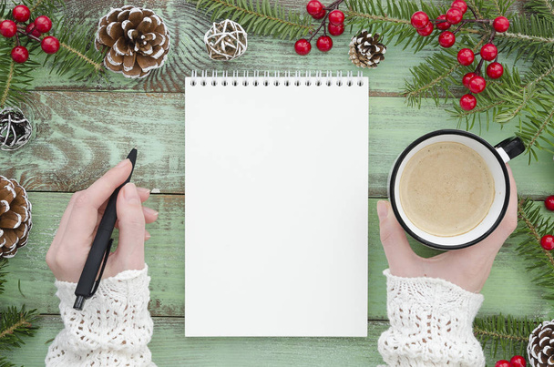 κάτοψη του κορίτσι χέρι εκμετάλλευση στυλό και σημειωματάριο μακέτα σε πράσινο φόντο ξύλινη καφέ. Χριστούγεννα, Χειμώνας, Πρωτοχρονιά, Χριστούγεννα διακοπές Εποχιακοί Χαιρετισμοί κάρτα. Μοντέρνα επίπεδη θέσει σχεδιασμού - Φωτογραφία, εικόνα
