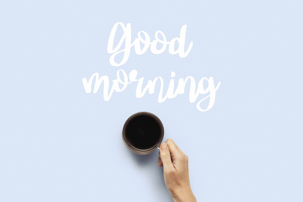 Hand hält eine Tasse mit heißem Kaffee auf blauem Hintergrund. Frühstückskonzept mit Kaffee oder Tee. Guten Morgen, Nacht, Schlaflosigkeit. flache Lage, Draufsicht. - Foto, Bild