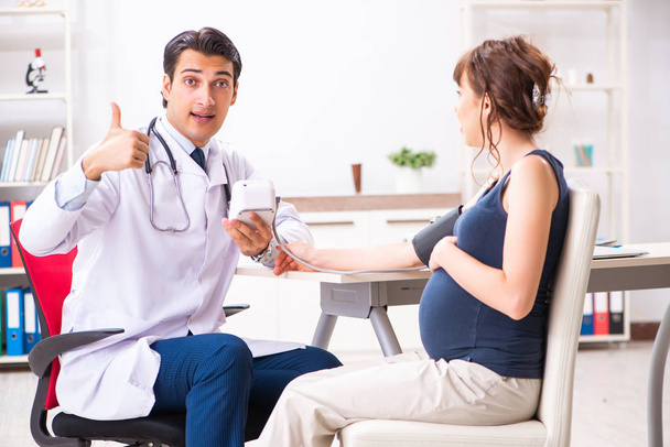 Junger Arzt überprüft Blutdruck von Schwangeren - Foto, Bild
