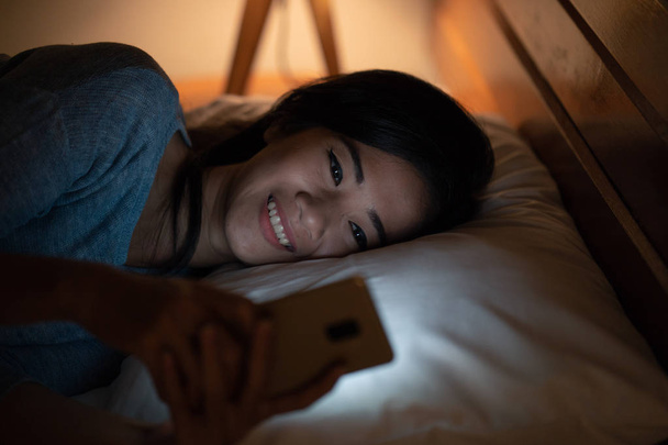 asian woman with smart phone while laying on bed - Foto, afbeelding