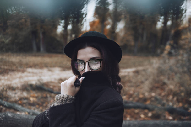A girl has a programmatic code reflected in her glasses. She covers her face with the coat's collar and stands on a forest background. - Foto, Bild