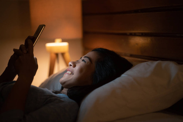 asian woman with smart phone while laying on bed - Photo, Image