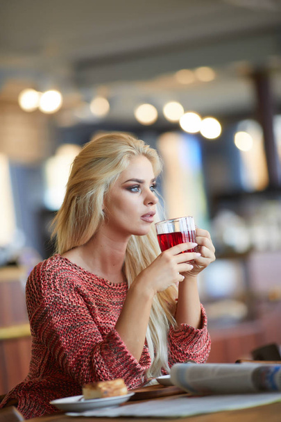 Blonde woman  looking through window while drinking tea sitting in cafe - Foto, Imagem