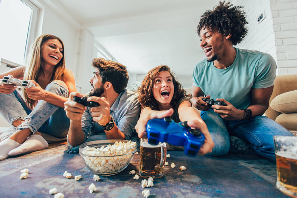 Группа друзей вместе играют в видеоигры дома, веселятся. - Фото, изображение
