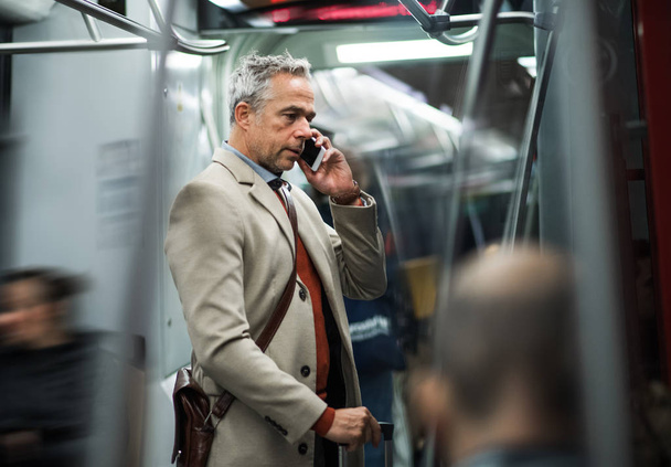 Mature businessman with smartphone travelling by subway in city. - Photo, image