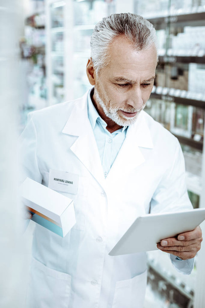 Attentive gray-haired man reading prescription on tablet - 写真・画像