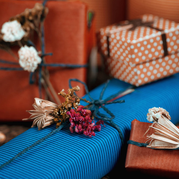 Composition carrée avec des boîtes-cadeaux enveloppées dans du papier de couleur naturelle, attachées avec de la ficelle, décorées de fleurs séchées
.   - Photo, image