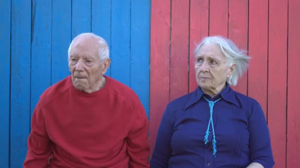 Důchodci na eco dřevěné pozadí. Důchodci oblečená v růžovém a modré se smutně dívá. Jsou unavení a staré. Jedinečné ekologické dřevěné pozadí dvou barev (růžové a modré). - Záběry, video