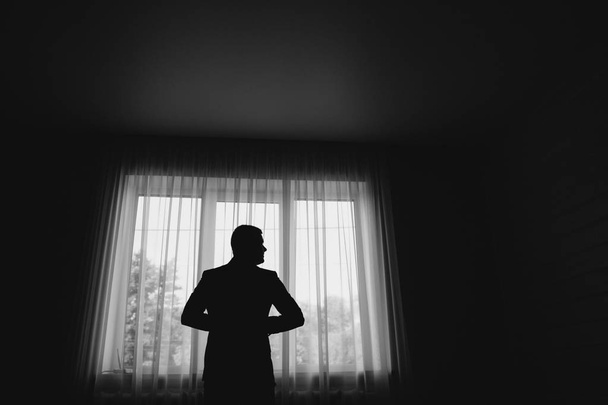 Man stand in front of window. Silhouette of young man. Black and white picture - Photo, Image