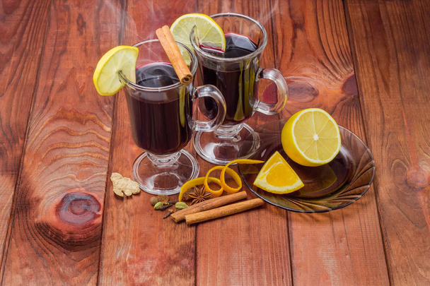Muokattu viini kahdessa lasimukissa sitruunaviipaleella ja mausteilla sen valmistamiseksi tummalla värillisellä puisella maalaispöydällä
 - Valokuva, kuva