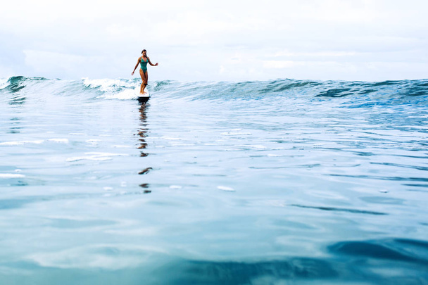 beautiful surfer girl riding on a board in the ocean on bali island - Фото, изображение