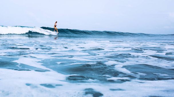 beautiful surfer girl riding on a board in the ocean on bali island - Foto, Imagen