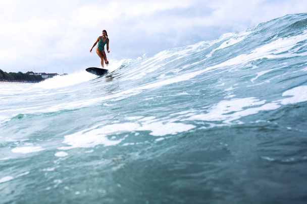 beautiful surfer girl riding on a board in the ocean on bali island - Photo, Image