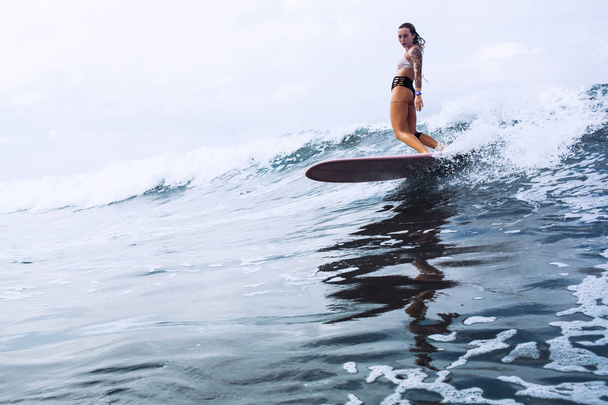 beautiful surfer girl riding on a board in the ocean on bali island - Photo, image
