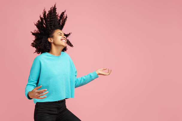 Portrait of excited african american young woman with bright smile dressed in casual clothes dance with invisible guitar over pink background. - Foto, immagini