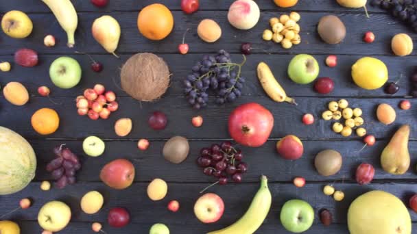 Vruchten op zwarte ecologische achtergrond. Bovenaanzicht. Diverse vruchten bevinden zich op zwarte houten eco achtergrond. Mannen handen nemen meloen uit eco-tabel. Hier zijn: bananen, citroen, kersen, sinaasappels, mandarijnen, perziken, peren. - Video