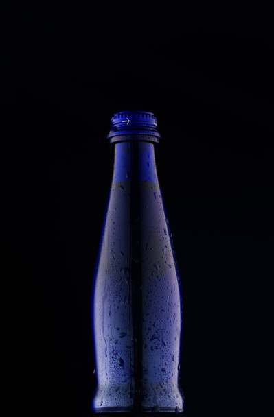 Μπλε γυάλινο μπουκάλι πυροβολήθηκε σε ένα μπλε φόντο στο φως - Φωτογραφία, εικόνα