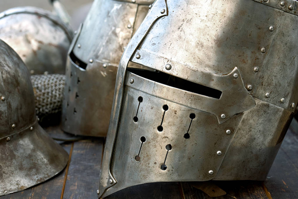 Стальные средневековые шлемы с разрезами на глазах на столе
 - Фото, изображение
