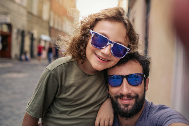 Smiling father and young son wearing sunglasses and taking a selfie while enjoying a day in the city together - 写真・画像