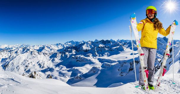 Retrato de menina feliz sentada na neve com esqui no inverno, pista de esqui no fundo
. - Foto, Imagem