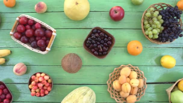 Vruchten op groene ecologische achtergrond. Bovenaanzicht. Diverse vruchten bevinden zich op de achtergrond van de groene houten eco. Sommige vruchten zijn in houten manden. Hier zijn: druiven, sinaasappels, pruimen, kiwi, peren, kokos, bananen, meloen, pruimen, granaatappel, perziken. - Video