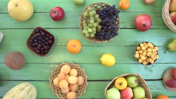 Ovoce na ekologické pozadí zelené. Pohled shora. Různé druhy ovoce jsou umístěny na pozadí zelené dřevěné eco. Některé plody jsou v dřevěných košů. Zde jsou: hrozny, pomeranče, švestky, kiwi, hrušky, kokos, banány, meloun, švestky, granátového jablka, broskve. - Záběry, video