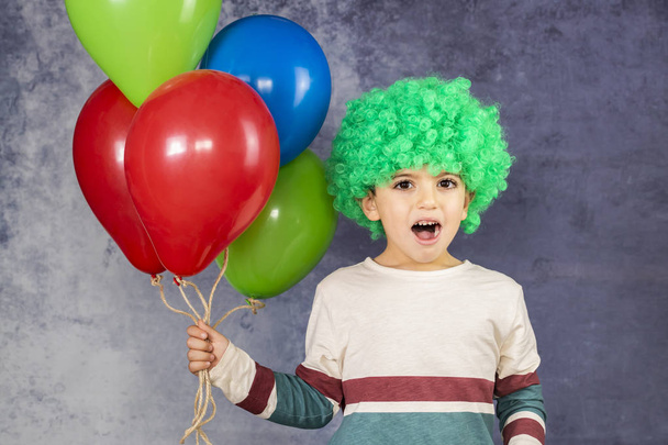 Μικρό αγόρι με μια πράσινη περούκα κρατώντας ένα πολύχρωμο μπαλόνια - Φωτογραφία, εικόνα