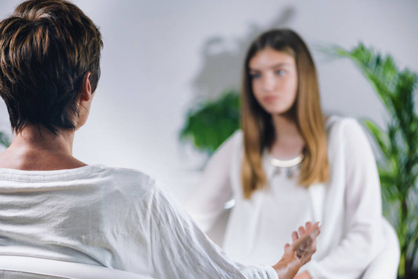 Female Theta healing therapist performing alternative therapy treatment with young woman patient. Therapist and patient talking. Energy healing concept. Wearing white clothes. - Photo, Image