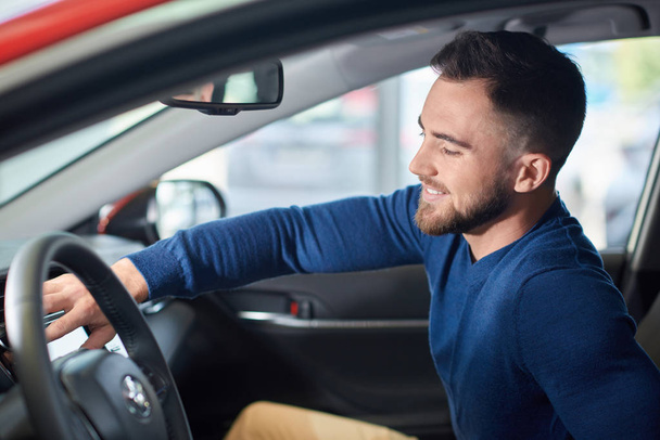 Brunette man with beard in blue sweater sitting in new car. - Photo, Image