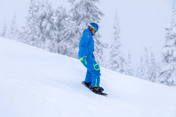 Ρωσία, Sheregesh 2018.11.18 επαγγελματίας snowboarder σε μπλε αθλητικά είδη και στολή σκι κατάβασης στο χιονισμένο sunny ψηλά βουνά. Θαμπάδα, μαλακή εστίαση, το αντικείμενο σε κίνηση. Freeride έννοια - Φωτογραφία, εικόνα
