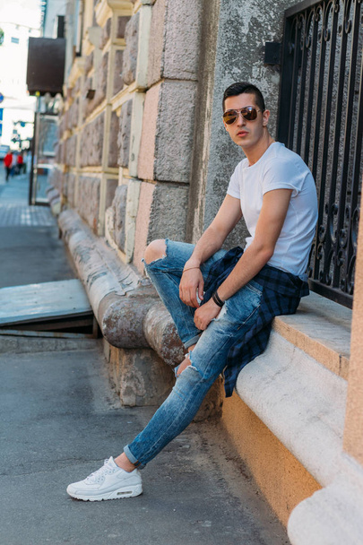 Attractive, sexy guy standing on the street in sunglasses. self-confidence, flatulence and arrogance.model, posing, portrait of a young man - Foto, Imagen
