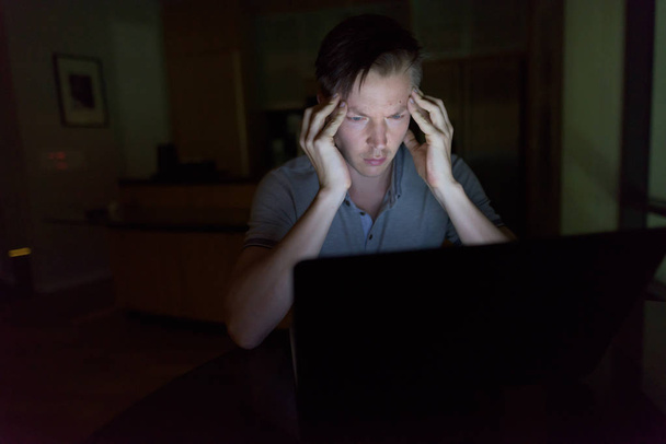 Όμορφος νεαρός που χρησιμοποιούν φορητό υπολογιστή στο σκοτεινό σαλόνι - Φωτογραφία, εικόνα