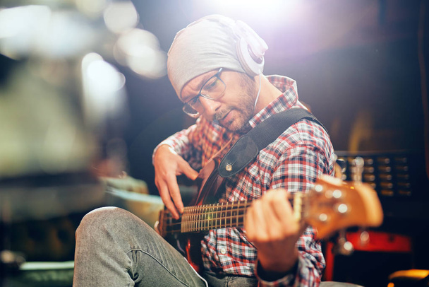 Κοντινό πλάνο του νεαρός μουσικός παίζοντας μπάσο κιθάρα με ακουστικά στα αυτιά. - Φωτογραφία, εικόνα