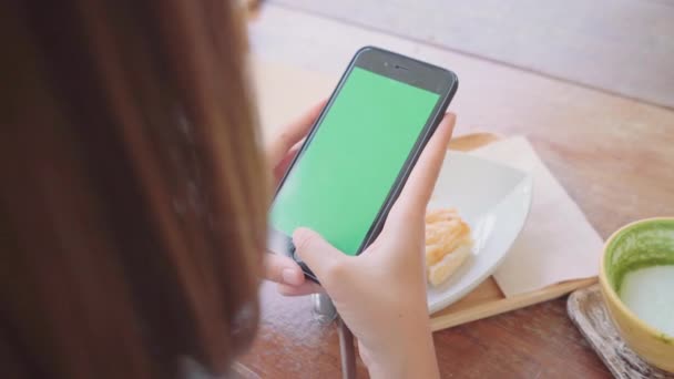 若いアジアの女性は、緑色の画面で黒の携帯電話のデバイスを使用します。カフェで座っている間ページをスクロールするスマート フォンを保持しているアジア女性。クロマ キー. - 映像、動画