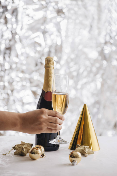 menselijke hand met glas champagne tijdens Nieuwjaar viering op zilver glitter achtergrond - Foto, afbeelding