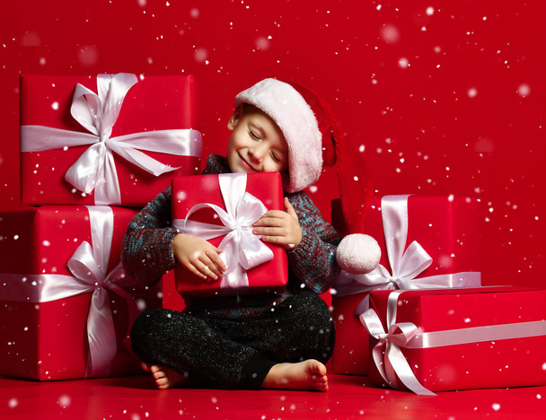 Smiling funny child in Santa red hat holding Christmas gift in hand. Christmas concept. - Photo, image