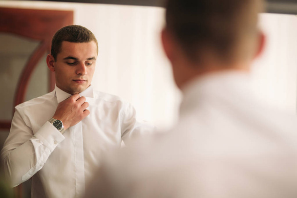 The groom is dressed at home in a suit. Cute groom posing for a photographer - 写真・画像