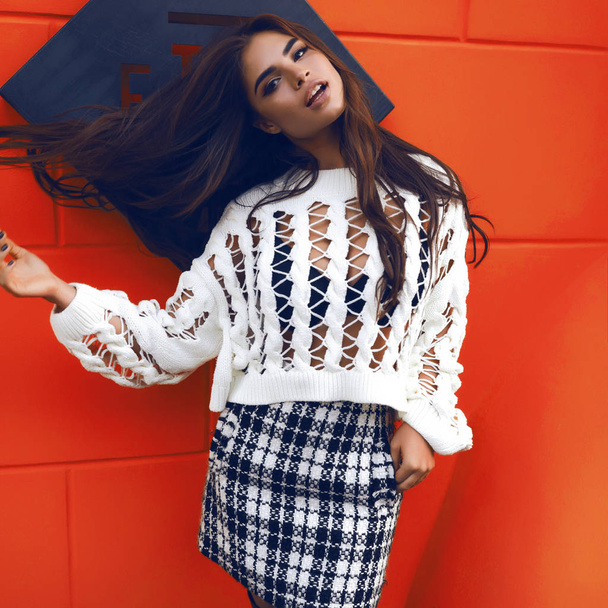 Picture of modern young woman in fashion clothes from autumn collection. Throwing hair up, bright makeup on the face. Trendy oversize blouse with holes, black underwear and checkered grey skirt - Φωτογραφία, εικόνα