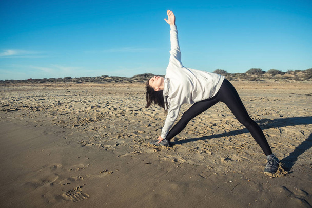 Yoga on the beach. Woman makes yoga Extended Triangle Pose, Utthita Trikonasana. Side view. - Foto, afbeelding