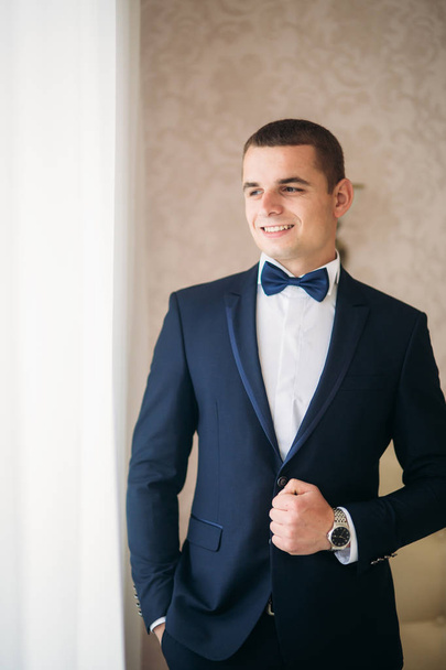 Handsome groom on a wedding day stand near the window - Foto, Imagen