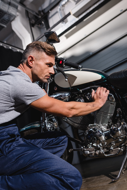 handsome adult mechanic fixing motorcycle engine in garage - 写真・画像