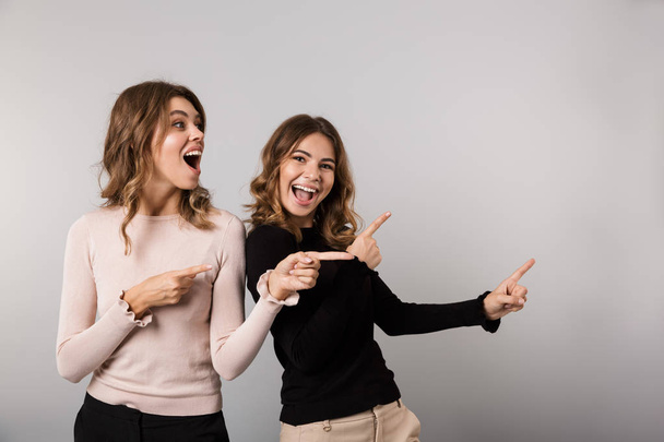 Image of two excited girls smiling and pointing fingers aside together isolated over gray background - Foto, Bild