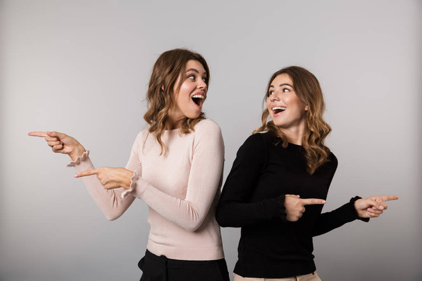 Image of two joyful women smiling and pointing fingers aside together isolated over gray background - Foto, afbeelding