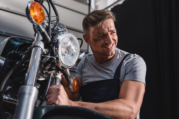 smiling mechanic checking motorcycle front wheel in garage - Foto, imagen